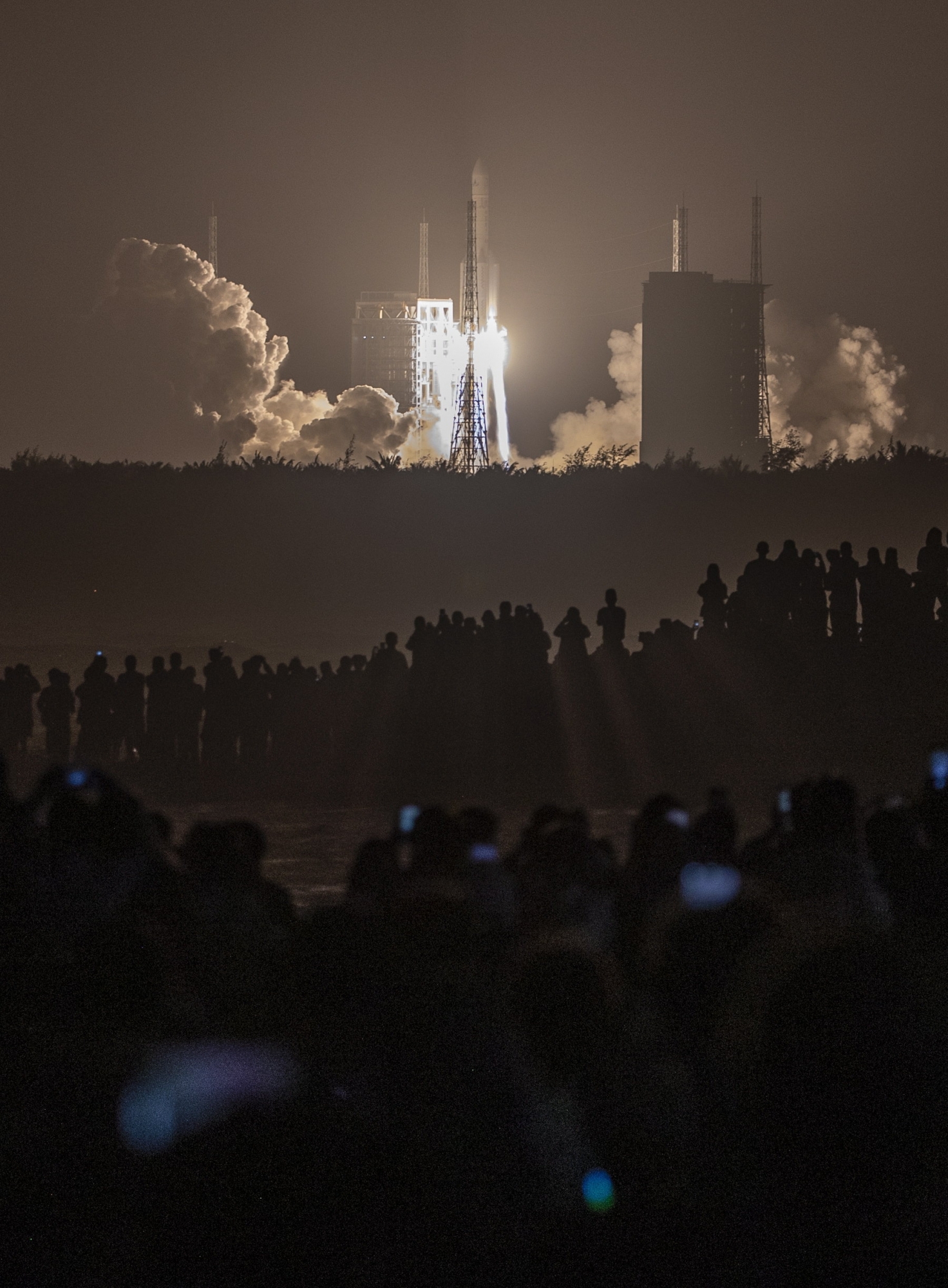 epa08838328 People watch a Long March 5 rocket carrying the Chang'e-5 lunar probe launching from the Wenchang Space Center in Wenchang, Hainan Island, China, 24 November 2020. China launched a mission to the Moon with an unmanned spacecraft on 24 November 2020 to bring back lunar rocks, the first country to attempt to retrieve material from the Moon in decades.  EPA/STR CHINA OUT ArcInfo