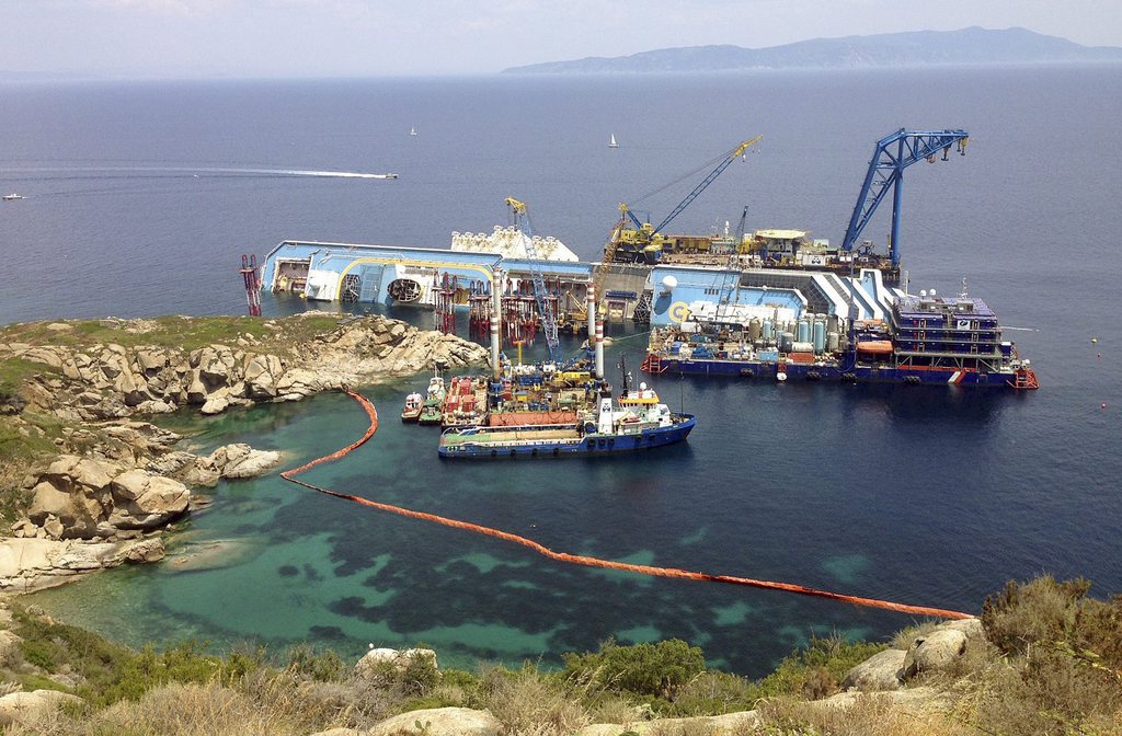 The Costa Concordia cruise ship lies on its side in the waters of the Tuscan island of Giglio, Italy, Monday, July 8, 2013. The luxury cruise ship ran aground off the coast of Tuscany on Jan 13, 2012, sending water pouring in through a 160-foot (50-meter) gash in the hull and forcing the evacuation of some 4,200 people from the listing vessel early. (AP Photo Paolo Santalucia)