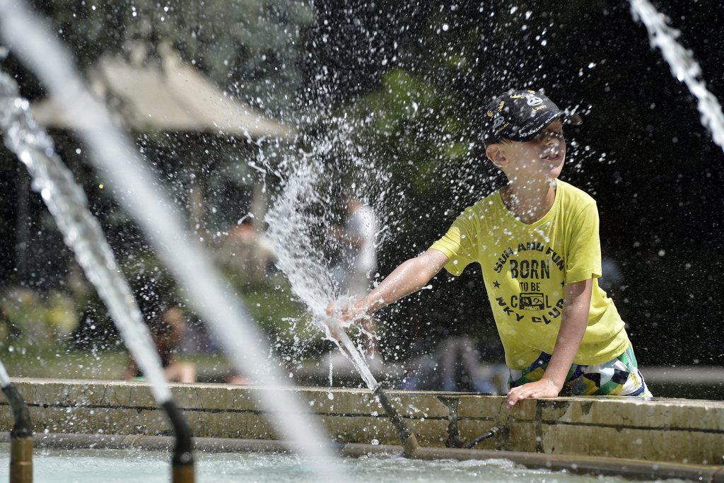 Un enfant s'amuse avec le jet de la fontaine du Jardin Anglais a Geneve, ce dimanche 14 juillet 2013. (KEYSTONE/Martial Trezzini)