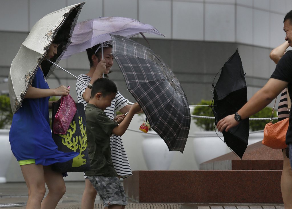 Tourists battle against strong wind near the waterfront in Hong Kong Wednesday, Aug. 14, 2013. Typhoon Utor lashed Hong Kong with wind and rain, closing down the bustling Asian financial center Wednesday before sweeping toward mainland China. (AP Photo/Vincent Yu)