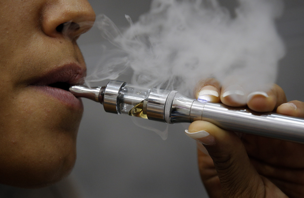 Kathleene, an electronic cigarette store employee, smokes an electronic cigarette in Paris, Tuesday, Oct. 8, 2013. The European Parliament voted to impose warning labels covering 65 percent of cigarette packs, rejecting a measure for blank packaging instead. Legislators also voted for new limits on advertising for electronic cigarettes, but rejected a measure that would have restricted them to medical use only. (AP Photo/Christophe Ena)