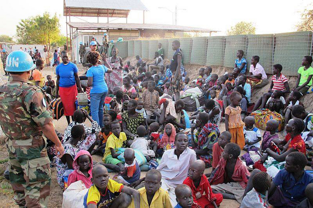 In this handout image provided by the United Nations Mission in South Sudan, taken on Tuesday, Dec. 17, 2013, a United Nation soldier stands guard as civilians arrive at the UNMISS compound adjacent to Juba International Airport to take refuge. Sporadic gunfire rang out in the capital, Juba, overnight as the military "cleared out remnants" of a faction of soldiers accused of mounting a coup attempt, the country's foreign minister said Tuesday amid an ongoing hunt for the former deputy president who is accused of leading the failed plot. (AP Photo/UNMISS/Rolla Hinedi)