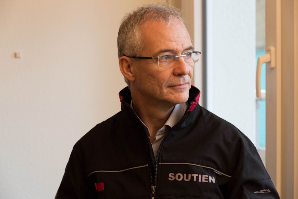 Daniel Pétremand, ici dans son bureau d'aumônier du CHUV, avec le gilet qu'il porte lors d'interventions. Le mot soutien s'y lit en blanc.