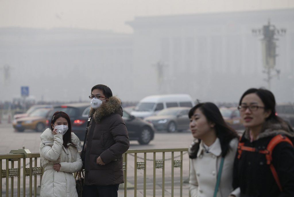 epa03980638 A Chinese couple (L) wears protective masks while going around the Tiananmen Square, which is seen with a hazy atmosphere around the Great Hall of the People in Beijing, China, 07 December 2013. China's weather authorities issued an orange alert on 07 December as heavy smog covered central and eastern regions of the country including Jiangsu, Zhejiang, Anhui and Henan provinces, reports stated. Beijing's midday index on 07 December had risen to a 'severely polluted' 303 micrograms per cubic meter, which is a measure of concentration of harmful fine particles in the air.  EPA/ROLEX DELA PENA