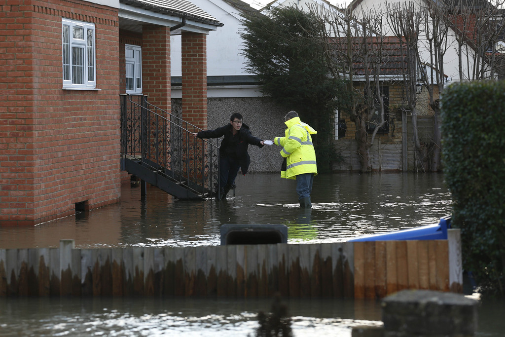 A man hands a piece of paper to a resident of a flooded house at Wraysbury, England, Monday, Feb. 10, 2014. The River Thames has burst its banks after reaching its highest level in years, flooding riverside towns upstream of London. Residents and British troops had piled up sandbags to protect properties from the latest bout of flooding, but the river overwhelmed their defenses Monday, leaving areas including the center of the village of Datchet underwater. (AP Photo/Sang Tan)