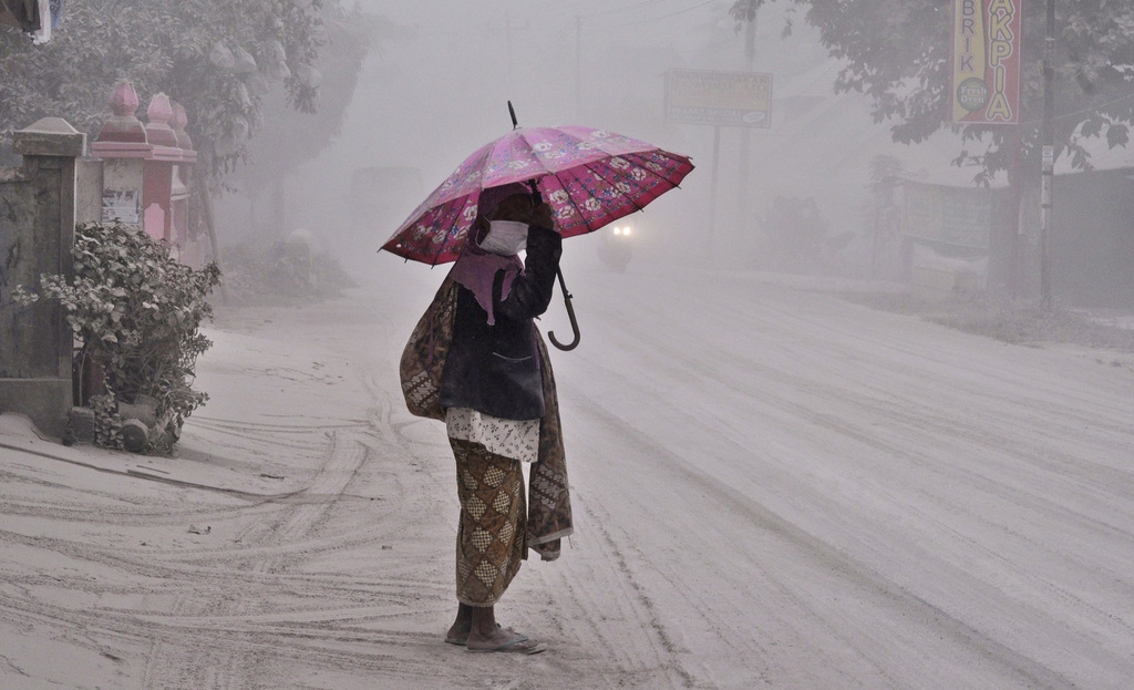 A women walks on  a road covered with volcanic ash following an eruption of Mount Kelud, in Yogyakarta, Indonesia, Friday, Feb 14, 2014. Volcanic ash from a major eruption in Indonesia shrouded a large swath of the country's most densely populated island on Friday, closed three international airports and sent thousands fleeing. (AP Photo/Slamet Riyadi)