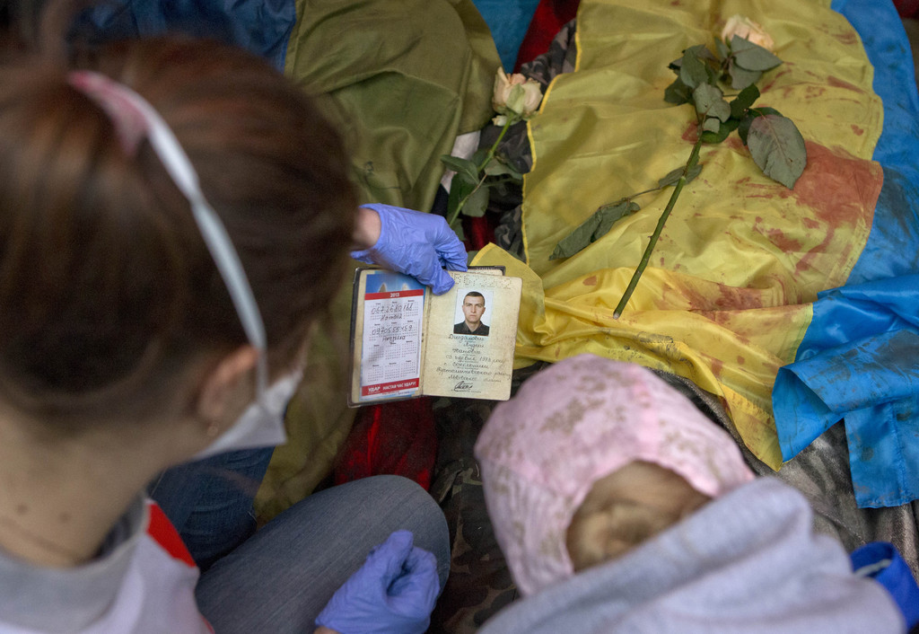 A paramedic looks at the identification document of a killed anti-government protester, in central Kiev, Ukraine, Thursday, Feb. 20, 2014. A brief truce in Ukraine's embattled capital failed Thursday, spiraling into fierce clashes between police and anti-government protesters. (AP Photo/Darko Bandic)