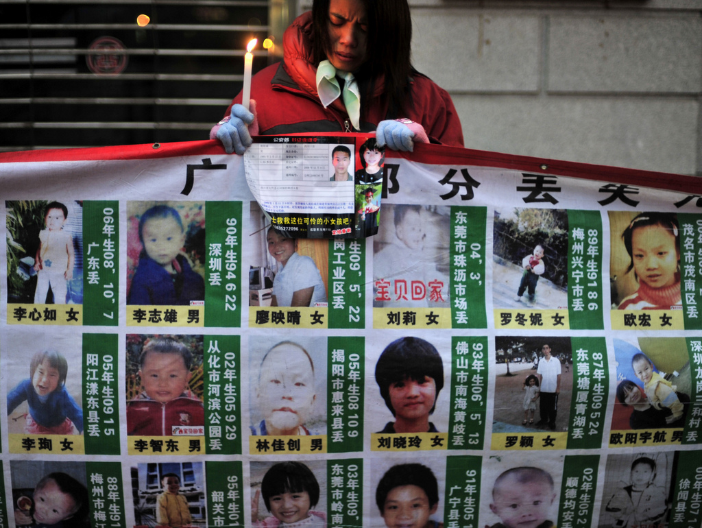 FILE - In this Jan. 24, 2010 file photo, a woman holds a candle behind a board showing photos of missing children during a campaign to spread the information to search for them in Wuhan, in central China's Hubei province. Chinese police have rescued 382 abducted babies and arrested 1,094 suspects in a national operation that busted four major Internet-based, baby-trafficking rings, the Public Security Ministry said Friday, Feb. 28, 2014. (AP Photo, File)  CHINA OUT