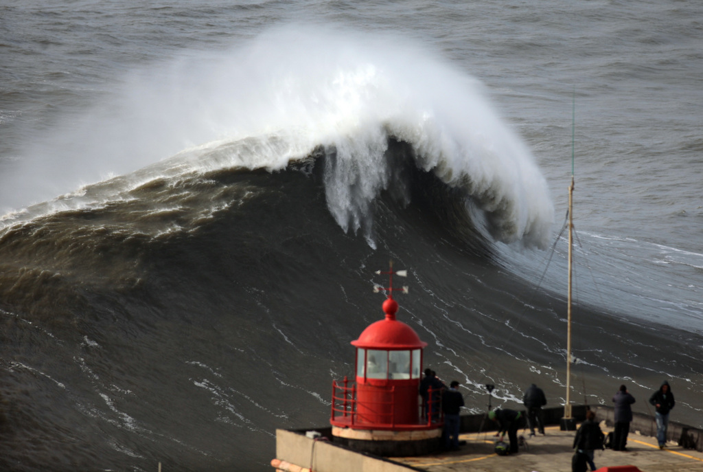 People watch huge waves approaching towards Nazare lighthouse, outside the fishing village of Nazare, in the central coast of Portugal, Sunday, Feb. 2, 2014. According to the Portuguese weather institute waves above six metres high were expected to hit the coastline and few ports, most of them in the north of the country, were closed due to the rough sea. (AP Photo/Francisco Seco)