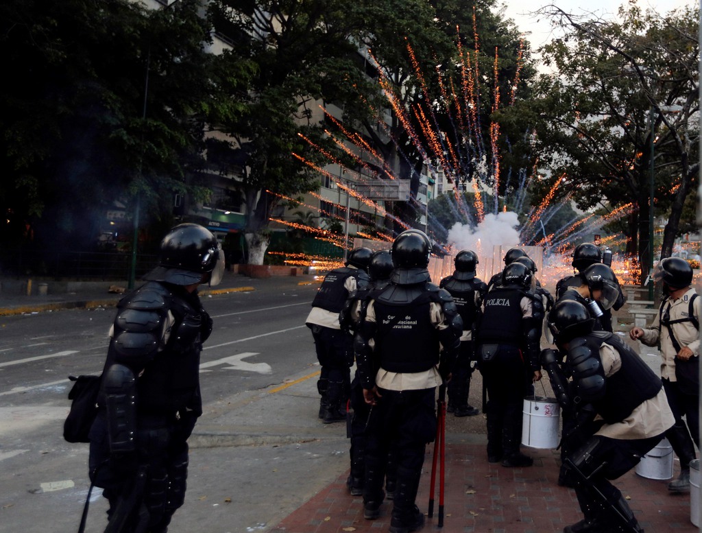 Bolivarian National Police officers take cover from exploding fireworks launched at them by anti-government demonstrators during clashes in Caracas, Venezuela, Thursday, March 6, 2014. A National Guardsman and a civilian were killed Thursday in a clash between residents of a Caracas neighborhood and armed men who tried to remove a barricade, Venezuelan officials said. (AP Photo/Fernando Llano)