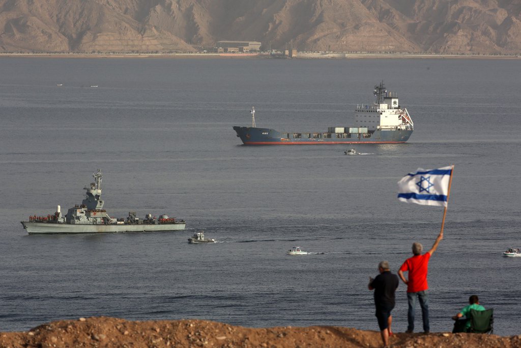 epa04115494 People wave an Israeli flag as the Klos-C cargo vessel (B) accompanied by Israeli Navy ships approaches the port of Eilat in the Red Sea, Israel, 08 March 2014. Israel on 05 March had intercepted a cargo vessel in the Red Sea carrying dozens of advanced rockets. Israel believes the missiles were meant to be delivered to militants in the Gaza Strip, as they said they had been tracking the missiles movements for months. The Syrian-made M-302 rockets have a range of up 160 kilometres with warheads of up to 150 kilogrammes, Israeli officials said.  EPA/ABIR SULTAN
