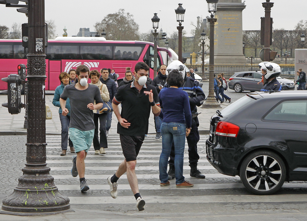 Two joggers wearing protective masks run past a Police officer controlling a vehicle on the Concorde square in Paris, Monday, March 17, 2014. Cars with even-numbered license plates are prohibited from driving in Paris and its suburbs Monday, following a government decision over the weekend.  Paris is taking drastic measures to combat its worst air pollution in years, banning around half of the city's cars and trucks from its streets in an attempt to reduce the toxic smog that's shrouded the City of Light for more than a week. (AP Photo/Remy de la Mauviniere)