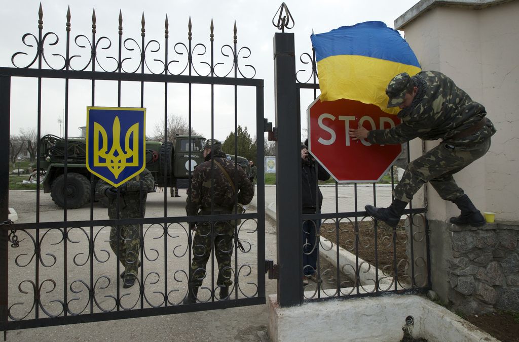 Un soldat ukrainien accroche le drapeau national sur la grille de la base de Belbek, en Crimée. La base est encerclée par les forces russes. 