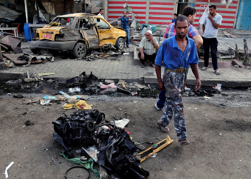 Iraqi civilians gather around damages in the aftermath of a car bombing in Baghdad's Sadr City, Iraq, Thursday, May 29, 2014. A series of bombings and attacks across Iraq killed and wounded scores of people Wednesday, authorities said, as politicians prepared to start negotiations to form a new government following parliamentary elections. (AP Photo/Karim Kadim)