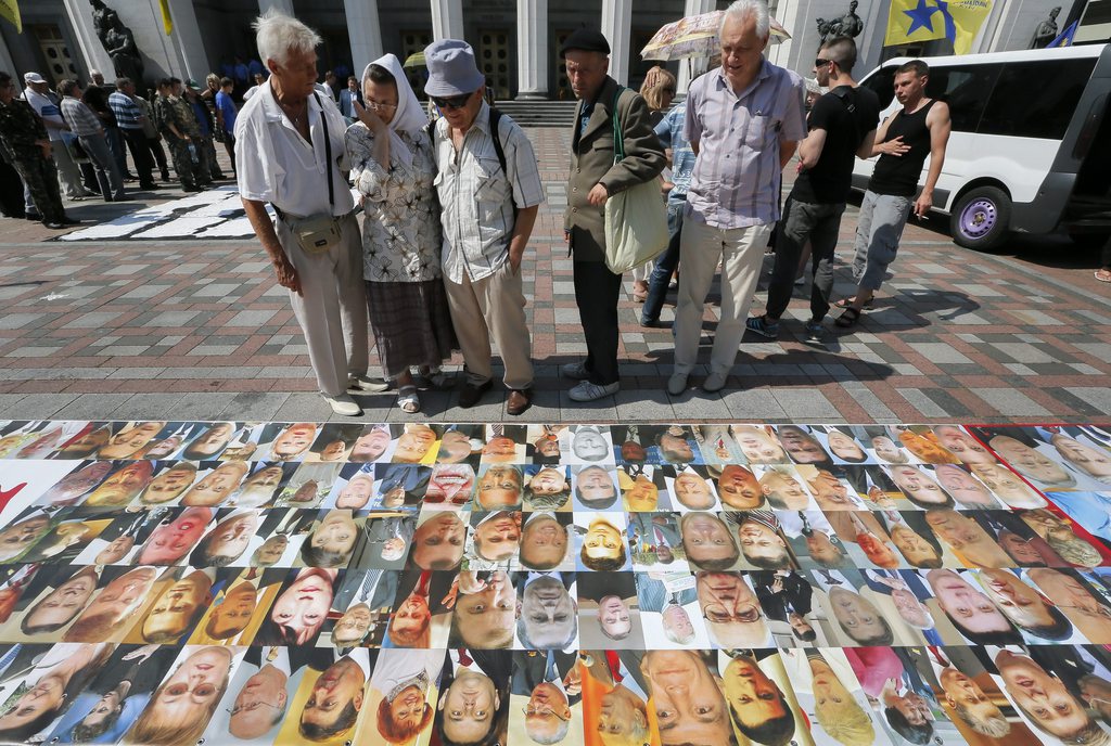 epa04336564 Ukrainians look at the portraits of Ukrainian lawmakers during their protest demanding for the parliament resignation in front of the parliament building in Kiev, Ukraine, 31 July 2014. Ukraine's parliament rejected Prime Minister Arseniy Yatsenyuk's decision to step down, awarding him a vote of confidence. Ukraine's parliament held an emergency session also to discuss the downing of flight MH17.  EPA/SERGEY DOLZHEKO