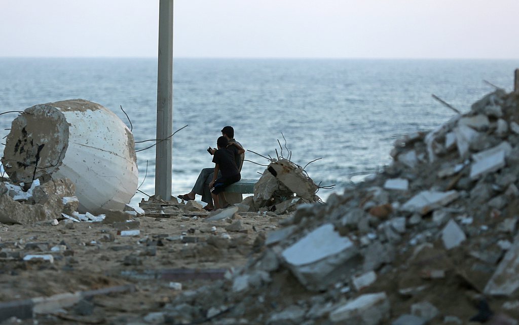 epa04341975 Palestinians sit between rubble at the beach of Gaza City, 05 August 2014. Israel pulled its last soldiers out of the Gaza Strip on 05 August after four weeks of fighting, as a  72-hour truce took effect at 8 am (0500 GMT) aimed at giving the sides three days to negotiate a longer-term deal. The Israeli army said its ground troops had withdrawn to the Israeli side of the border, where they would remain on alert and respond to any attacks.  EPA/MOHAMMED SABER
