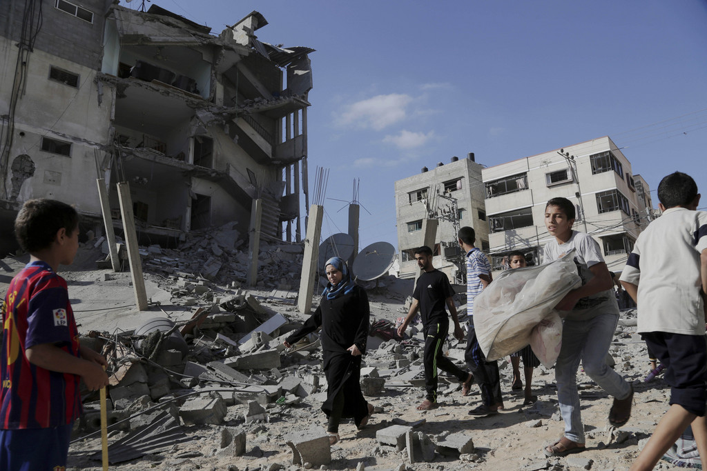 Palestinians walk as other salvage what he can from the rubble of a four-story building following an Israeli air strike in Gaza City, in the northern Gaza Strip, Friday, Aug. 8, 2014. Israel and Gaza militants resumed cross-border attacks on Friday after a three-day truce expired and Egyptian-brokered talks on a new border deal for blockaded Gaza hit a deadlock. (AP Photo/Adel Hana)