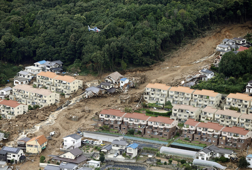 In this aerial photo, a rescue helicopter hovers  over an area devastated by a massive landslide in Hiroshima, western Japan, Wednesday, Aug. 20, 2014. A several people died and at least a dozen are missing after rain-sodden hills in the outskirts of Hiroshima gave way early Wednesday in several landslides. (AP Photo/Kyodo News) JAPAN OUT, MANDATORY CREDIT