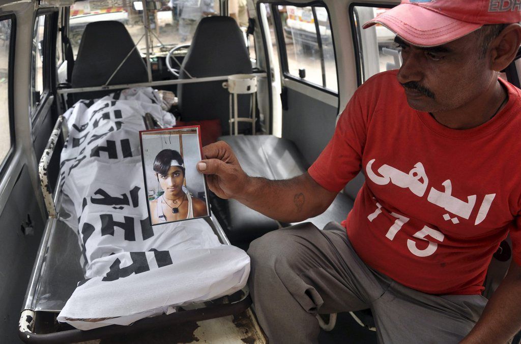 epa04336519 A rescue worker shows the picture of a victim who was drowned while swimming at the beach, as his body (L, back) is shifted from a mortuary, in Karachi, Pakistan, 31 July 2014. At least 19 persons were drowned while swimming at the beach during the Eid al-Fitr holidays.  EPA/SHAHZAIB AKBER