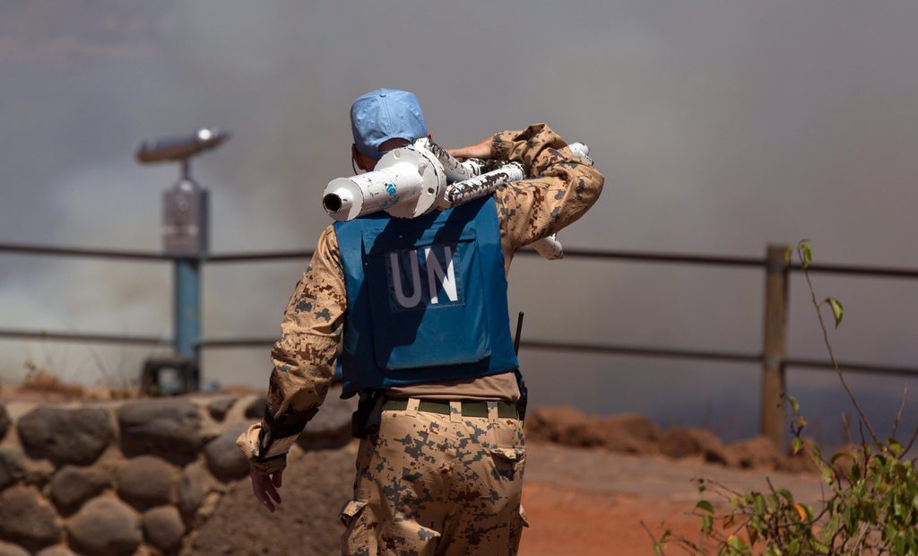 epa04370475 UN peacekeeper carrying equipments as  smoke rises in the background at the Syrian-Israeli border as a result of the fighting between the Syrian army and rebels over the control of the border crossing of Quneitra, the only official crossing between Israel and Syria, 27 August 2014. Media reports that the Syrian rebels managed to gain control over the border crossing. At least three rockets fired from Syria hit various locations in Israel's Golan Heights, a military spokeswoman confirmed, adding that the incident was unrelated to the ongoing hostilities with Hamas.  EPA/ATEF SAFADI