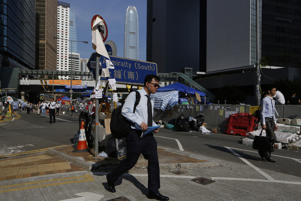 People walk to work on a main road in the occupied areas surrounding the government complex in Hong Kong Oct. 6, 2014. Hong Kong's civil servants returned to work and schools were reopening Monday as a massive pro-democracy protest that has occupied much of the city center for the week dwindled. (AP Photo/Kin Cheung)