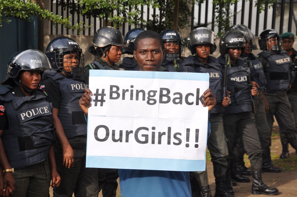 A man poses with a sign in front of police officers in riot gear during a demonstration calling on the government to rescue the kidnapped girls of the government secondary school in Chibok, in Abuja, Nigeria, Tuesday, Oct. 14, 2014. Scores of protesters marched chanting "Bring Back Our Girls" kidnapped six months ago by Boko Haram. (AP Photo/Olamikan Gbemiga)