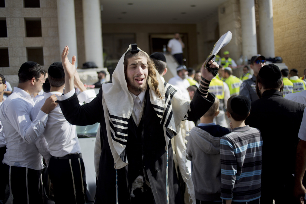 An ultra-Orthodox Jewish man prayers as Israeli rescue workers clean the scene of a shooting attack in a Synagogue in Jerusalem, Tuesday, Nov. 18, 2014. Two Palestinians stormed a Jerusalem synagogue on Tuesday, attacking worshippers praying inside with knives, axes and guns, and killing four people before they were killed in a shootout with police, officials said. (AP Photo/Ariel Schalit)