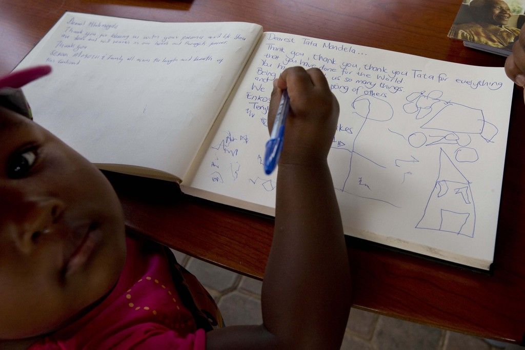 A child draws in the condolence register on a page where her mother left a message for "Tata" or "Father" Mandela at the Nelson Mandela Centre of Memory in Johannesburg, South Africa, Saturday Dec. 7, 2013. Flags were lowered to half-staff and people in black townships, in upscale mostly white suburbs and in South Africa's vast rural grasslands commemorated Nelson Mandela with song, tears and prayers on Friday while pledging to adhere to the values of unity and democracy that he embodied. (AP Photo/Peter Dejong)