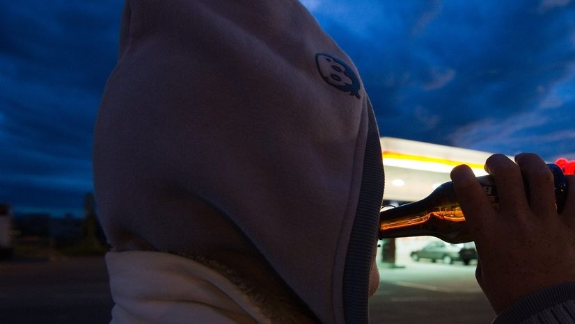 Un jeune boit de l'alcool devant une station service.