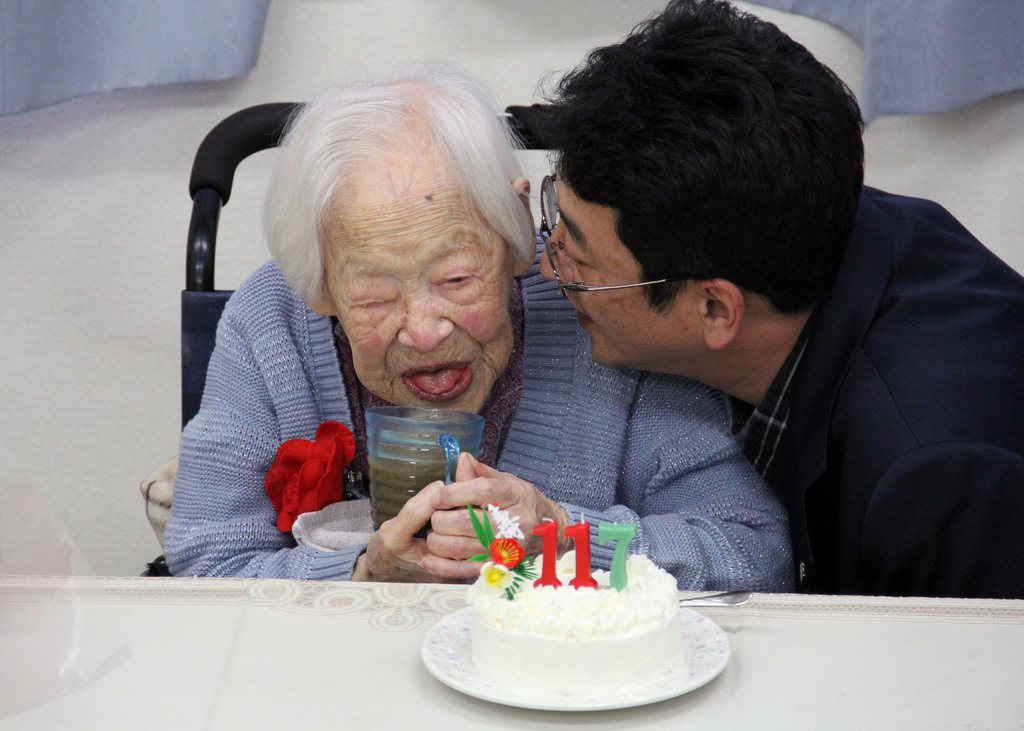 epa04648270 A handout picture provided by the Kurenai Nursing Home shows 117-year-old Japanese Misao Okawa (L) smiling before a birthday cake at the nursing home in Osaka, western Japan, 05 March 2015. Okawa, the world's oldest living person, turned 117 on 05 March. Okawa was born on March 5, 1898, the daughter of a kimono shop owner in Osaka. She now lives in a nursing care facility in the western Japanese city.  EPA/KURENAI NURSING HOME  HANDOUT EDITORIAL USE ONLY/NO SALES