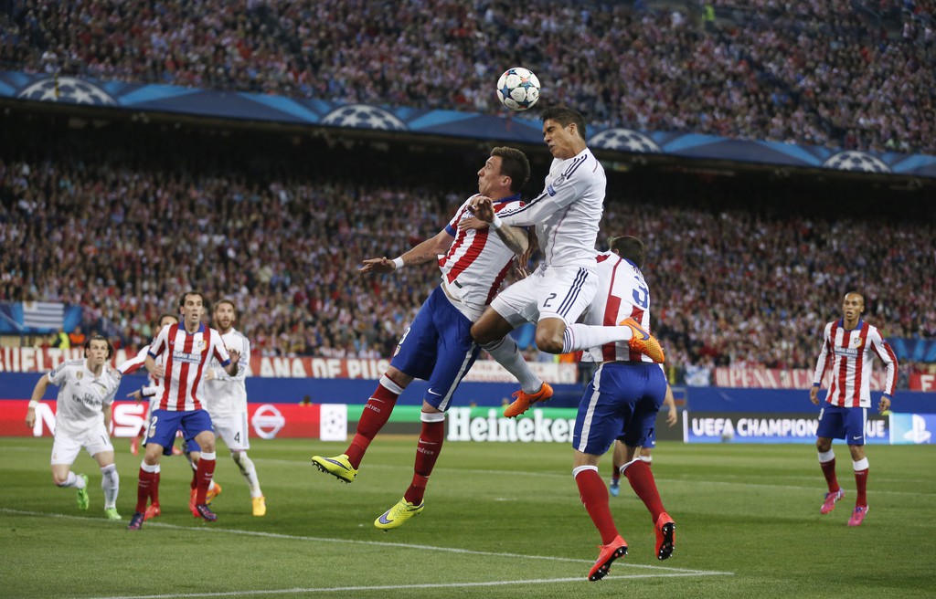 Atletico's Mario Mandzukic, center left, challenges Real Madrid's Raphel Varane, center right, during the Champions League quarterfinal, first leg soccer match between Atletico de Madrid and Real Madrid at the Vicente Calderon stadium in Madrid, Spain, Tuesday, April 14, 2015. (AP Photo/Daniel Ochoa de Olza)