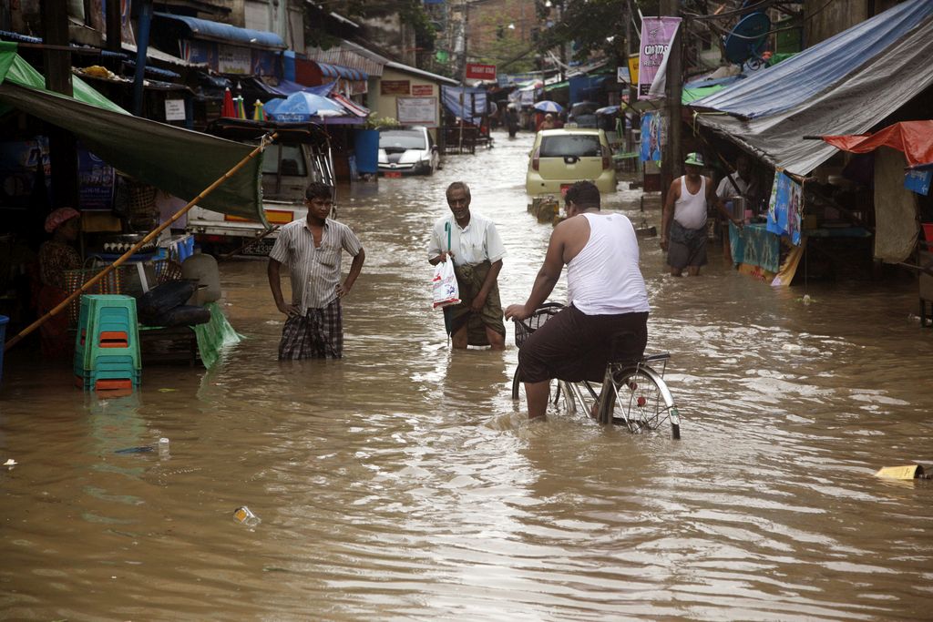 A man rides bicycle as pedestrians walk through a flooded street, caused by heavy rains Tuesday, July 28, 2015, Yangon, Myanmar. The State-run Kyemon daily reported Monday that flooding triggered by heavy monsoon rains falling on many parts of Myanmar had also damaged roads and bridges, including a 100-year-old bridge in northern Shan state Sipaw township. (AP Photo/Khin Maung Win)