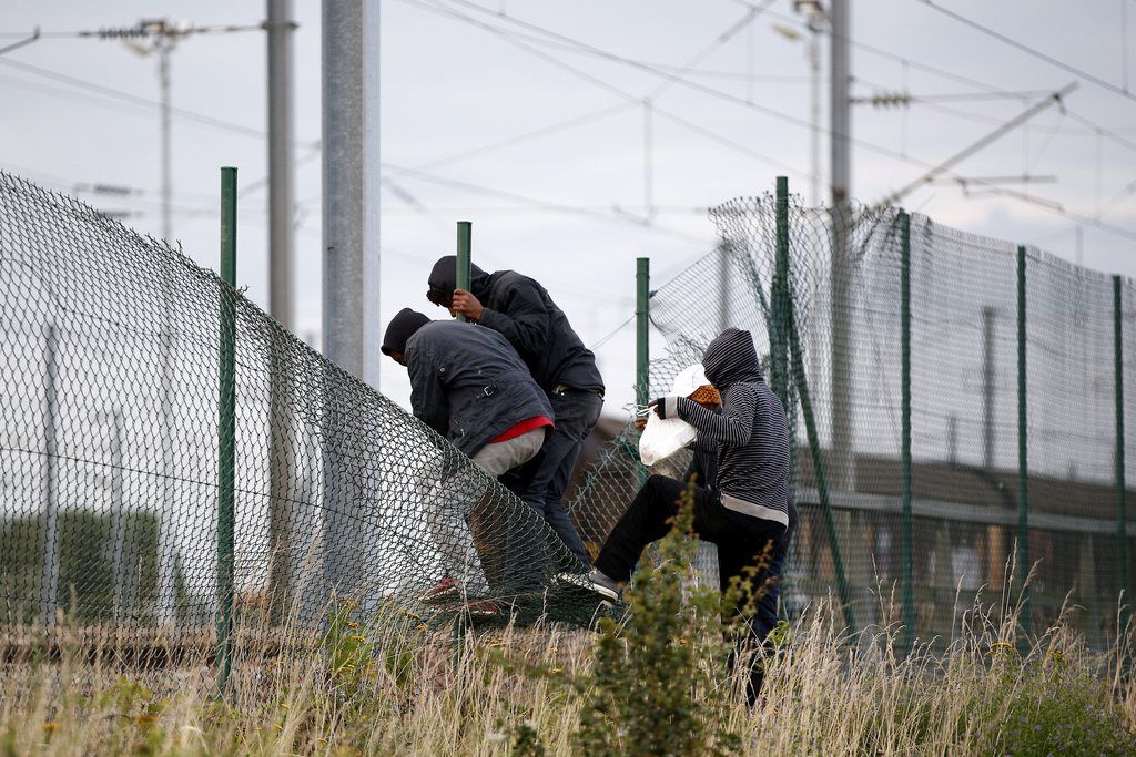 epa04865376 Migrants step over the fence as they try to catch a train to reach England, in Calais, France, 29 July 2015. A Sudanese man, between 25 and 30 years old, was crushed under a truck as up to 1,500 migrants tried to force their way into the tunnel, which links France and Britain under the English Channel. Since the beginning of the year there were more than 37,000 interceptions of migrants in Calais attempting to cross to England, the Eurotunnel operators said on 29 July.  EPA/YOAN VALAT