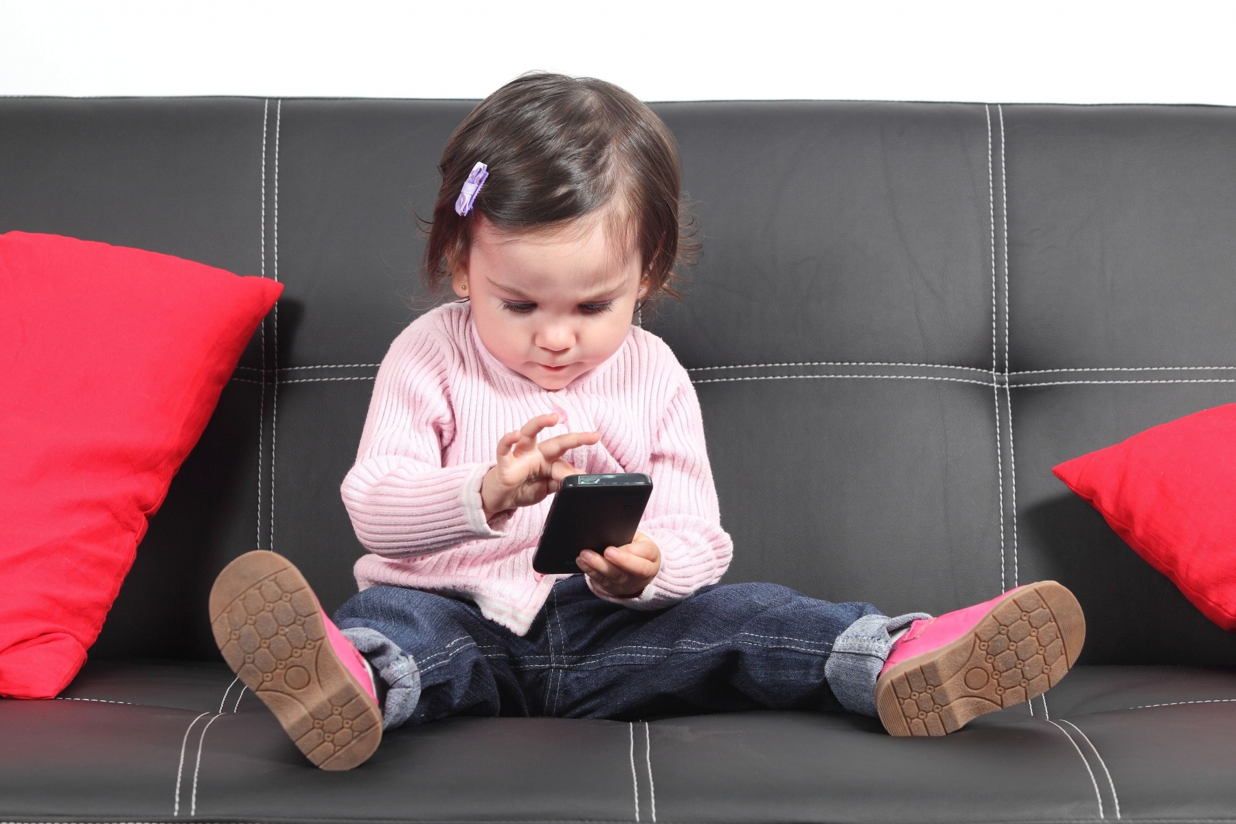 Casual baby sitting on a couch at home playing and touching a mobile phone Casual baby sitting on a couch touching a mobile phone