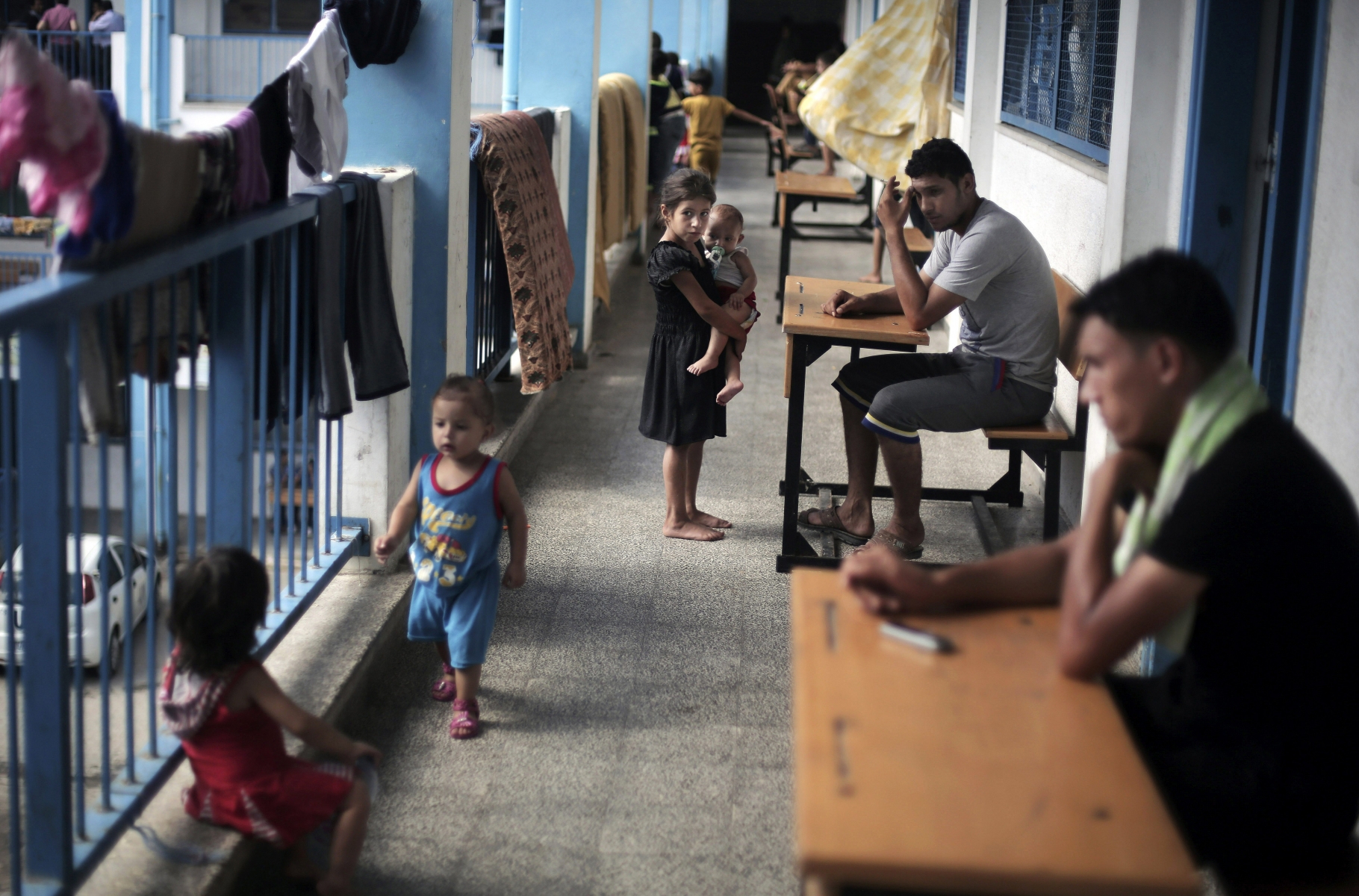 In this Wednesday, Sept. 3, 2014 photo, Palestinians sit outside the classrooms in a U.N. school where families live after their house was destroyed by Israeli strikes, in Gaza City. With nearly 100,000 Palestinians in Gaza having no home to go back to, the U.N.-run schools are still housing thousands just one week before the school year is scheduled to begin, posing a challenge to authorities. (AP Photo/Khalil Hamra)