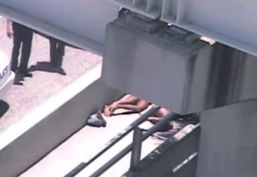 In this image taken from video, Miami police officers stand watch near a naked man, second from right, who was shot dead by a police officer when he refused to stop chewing on the face of the naked man next to him, partially obscured by a railing, on the MacArthur Causeway ramp onto Northeast 13th Street in Miami, Saturday, May 26, 2012. The victim was taken to a nearby hospital. Police say neither man's identity is known. (AP Photo/The Miami Herald)  MAGS OUT