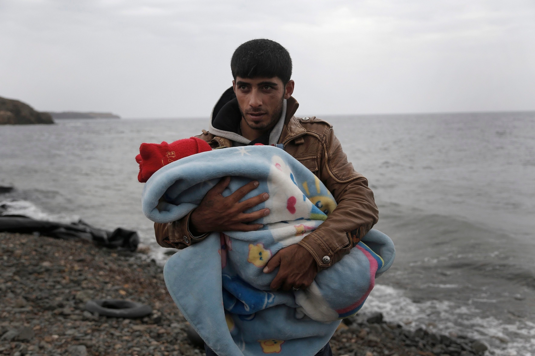epa04973104 A man holds his baby after arriving on a rubber dinghy on the island of Lesvos, having crossed the Aegean sea from Turkey, Greece, 11 October 2015. A recently agreed European Union plan to relocate tens of thousands of asylum seekers from Italy and Greece elsewhere in the bloc will start at the end of this week, a top EU official said 06 October. Lesbos - the third-largest Greek island and home to nearly 90,000 people - has been overwhelmed with migrants from Syria, Afghanistan and Iraq trying to reach Europe. More than 200,000 refugees arrived on the island this year alone, according to the UN refugee agency. Many of the refugees begin their journey to Lesbos across sparkling Aegean waters in Turkey.  EPA/YANNIS KOLESIDIS GREECE OUT GREECE MIGRATION REFUGEES CRISIS