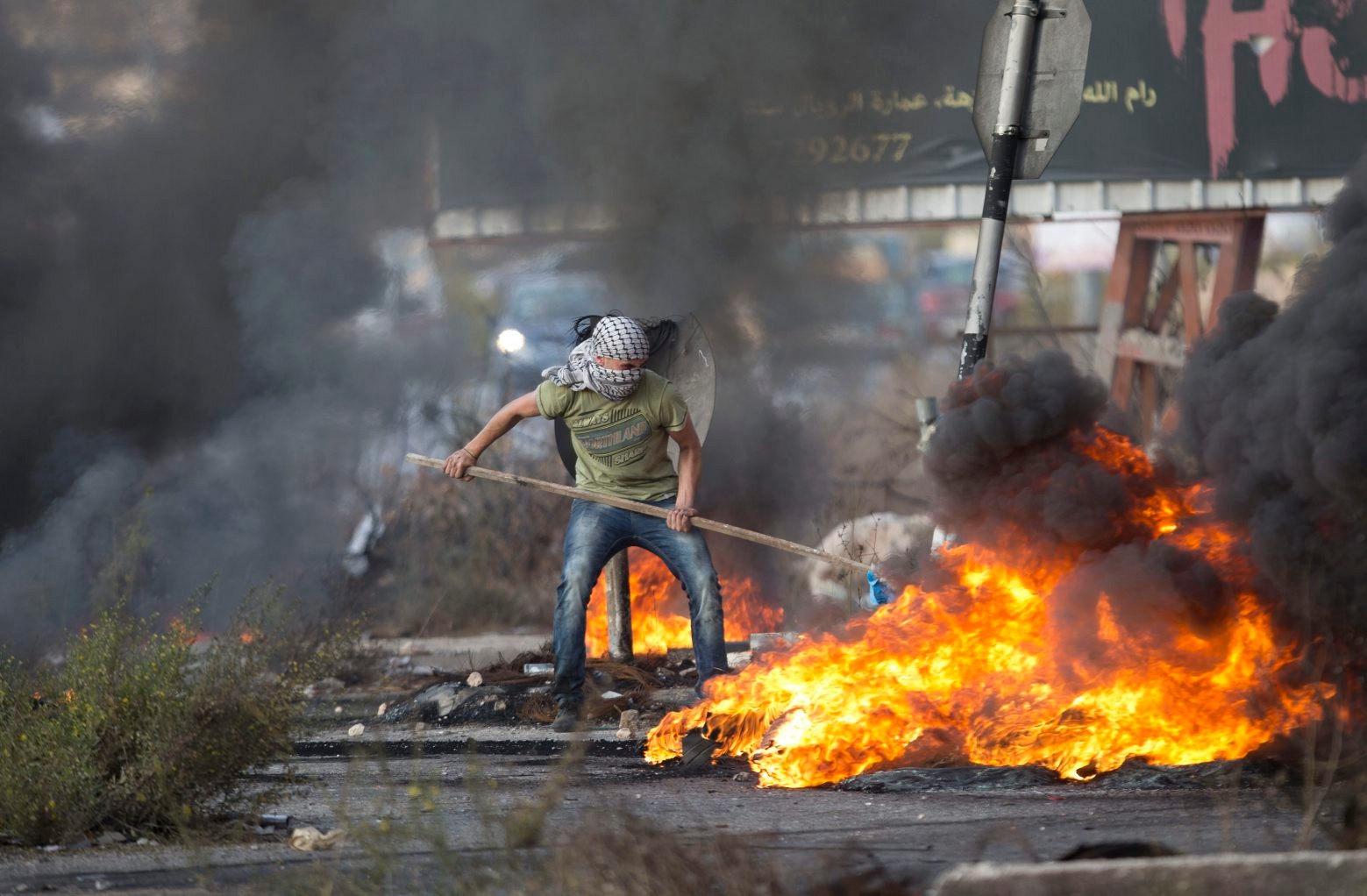 A Palestinian pushes burning tries during clashes with Israeli troops near Ramallah, West Bank, Tuesday, Oct. 13, 2015. A pair of Palestinian men boarded a bus in Jerusalem and began shooting and stabbing passengers, while another assailant rammed a car into a bus station before stabbing bystanders, in near-simultaneous attacks Tuesday that escalated a monthlong wave of violence. Three Israelis and two attackers were killed.  (AP Photo/Majdi Mohammed) Mideast Israel Palestinians