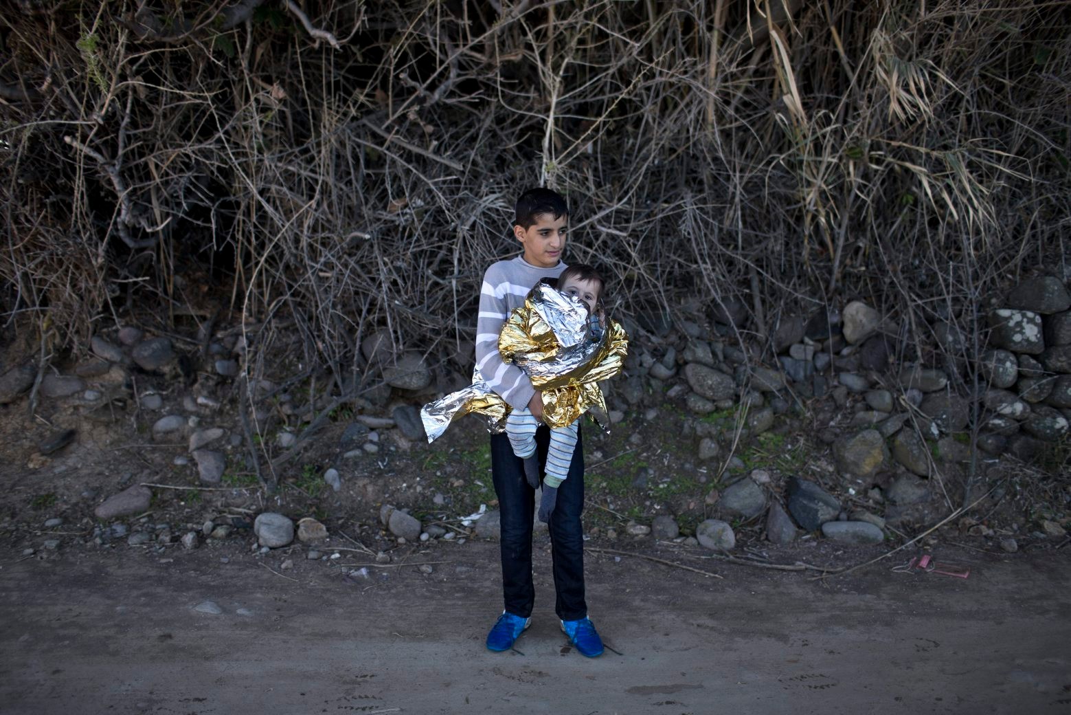 A youth holds a baby wrapped in an emergency blanket after people have disembarked a rubber boat that brought them from neighboring Turkey on the northern shore of Lesbos, Greece, Monday, Nov. 2, 2015. More than 300,000 people have traveled on dinghies and boats from nearby Turkey to Lesbos this year, with dozens dying along the way. (AP Photo/Marko Drobnjakovic) Greece Migrants