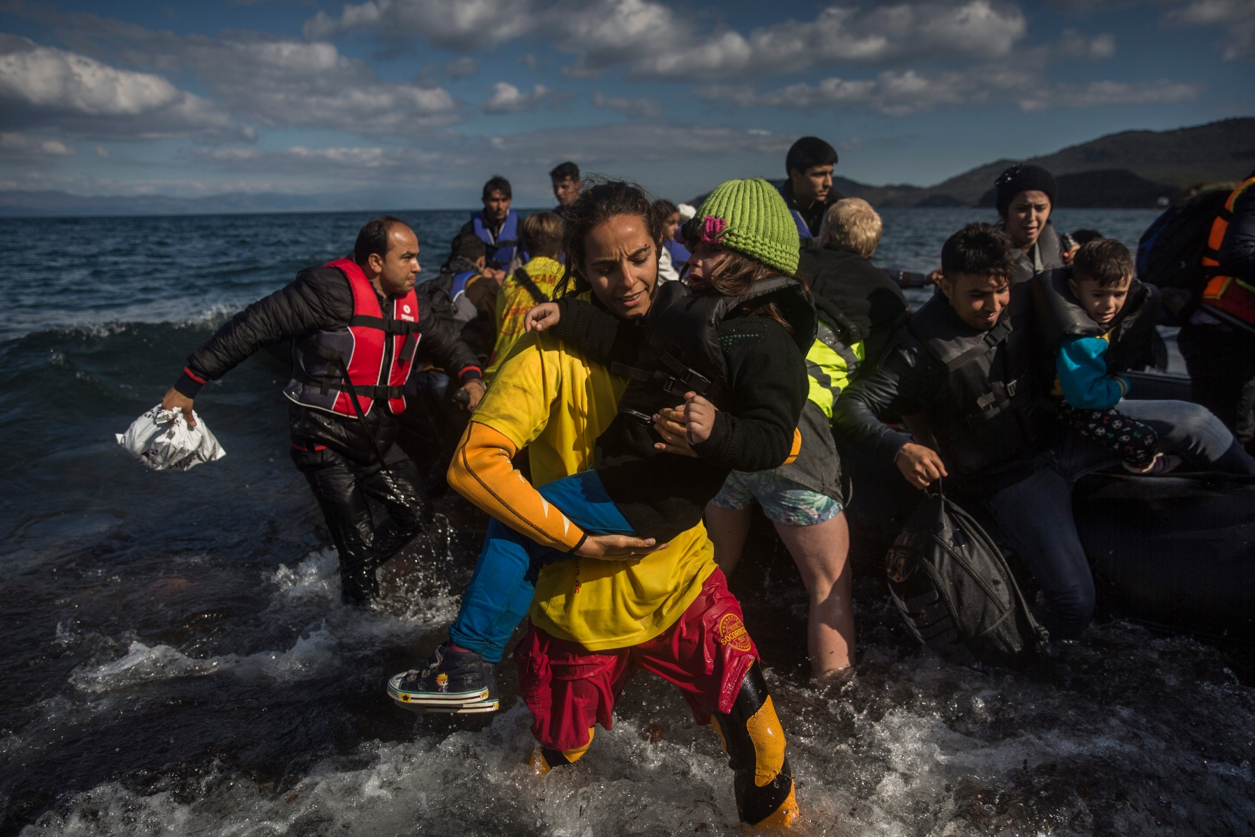 In this picture made on Sunday, Oct. 25, 2015, Fiorella Crotti  member of Spanish rescue group Proactiva Open Arms carries a young kid as migrants and refugees disembark from a dinghy after crossing the Aegean sea from Turkey to the Greek island of Lesbos.  As this Greek island struggles with a huge migrant surge, a close-knit group of volunteers, many from overseas, work alongside Greek fishermen to rescue people at sea, provide medical care and bring comfort and basic necessities.(AP Photo/Santi Palacios) Europe Migrants Helpers