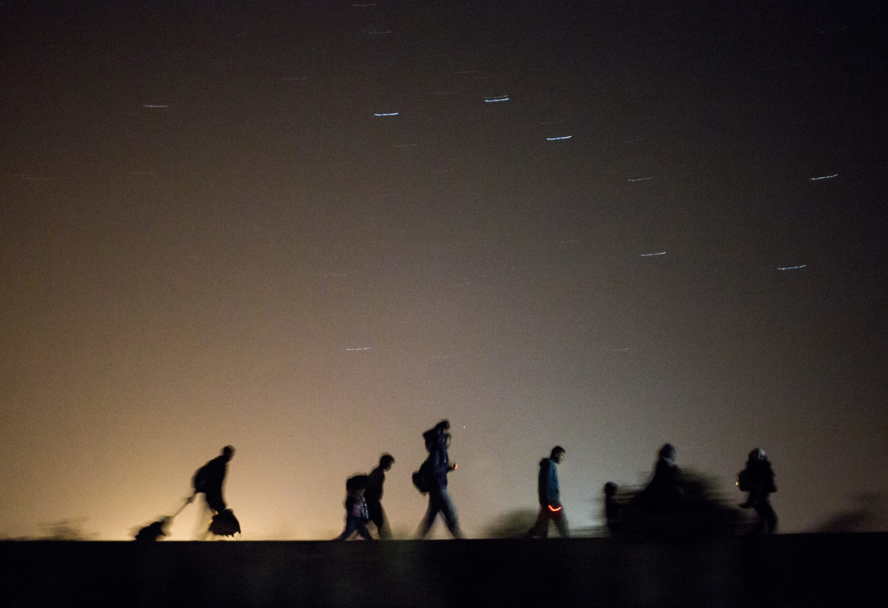 In this Sept. 13, 2015 photo taken with slow shutter speed migrants walk towards a checkpoint along the railway tracks connecting Horgos and Szeged near Roszke, in the vicinity of the border between Hungary and Serbia. (Balazs Mohai/MTI via AP)