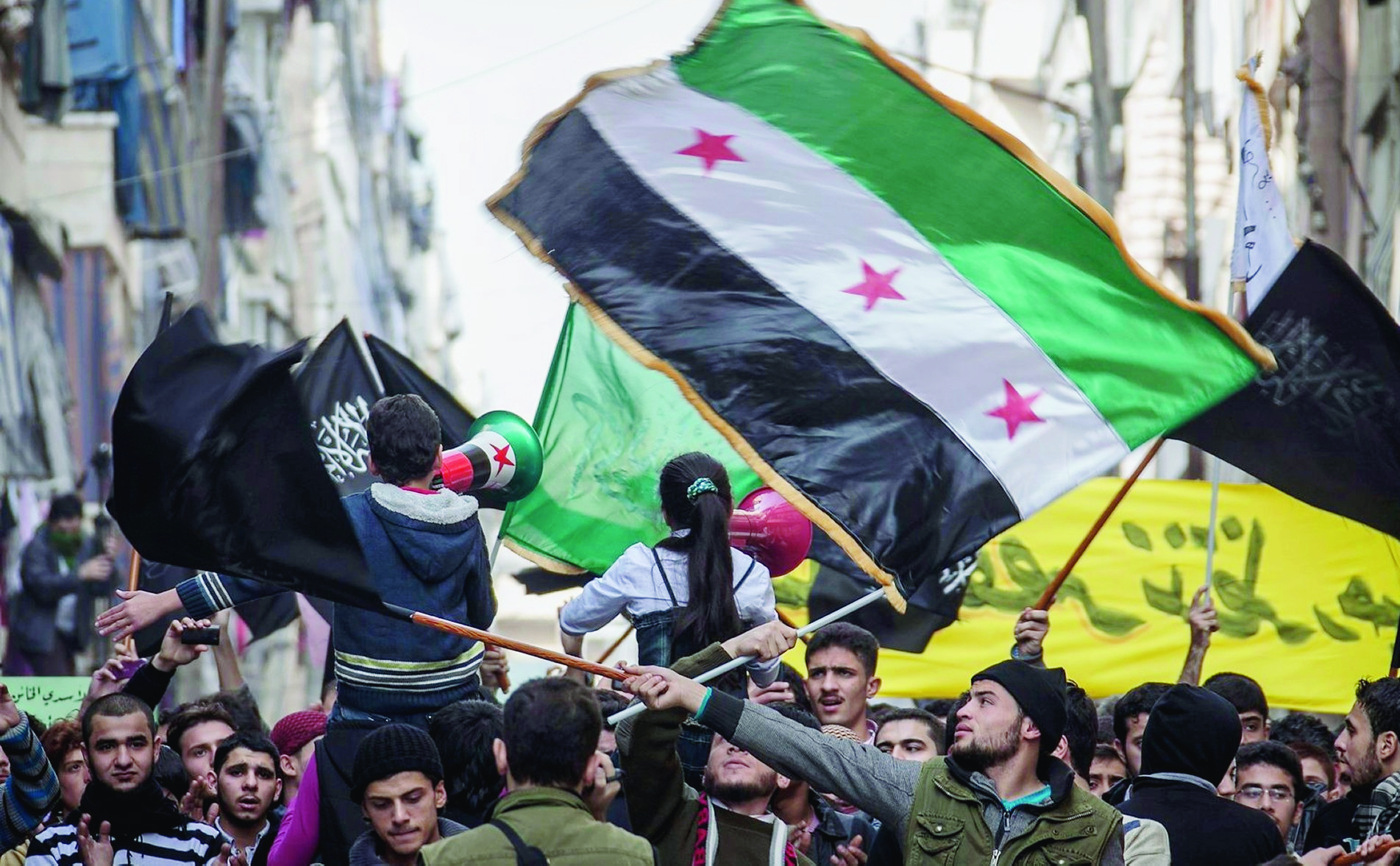 In this Friday, Nov. 30, 2012 photo, Syrians chant slogans and wave revolutionary flags during a demonstration after Friday prayers in the Bustan Al-Qasr district of Aleppo, Syria. After months of fighting, thousands of residents have returned to the city as they attempt to return to their daily lives while heavy fighting is still taking place along the front lines in the city. Public demonstrations have unfolded after several weeks of silence as residents demand an end to the violence in Aleppo. (AP Photo/Narciso Contreras) Mideast Syria