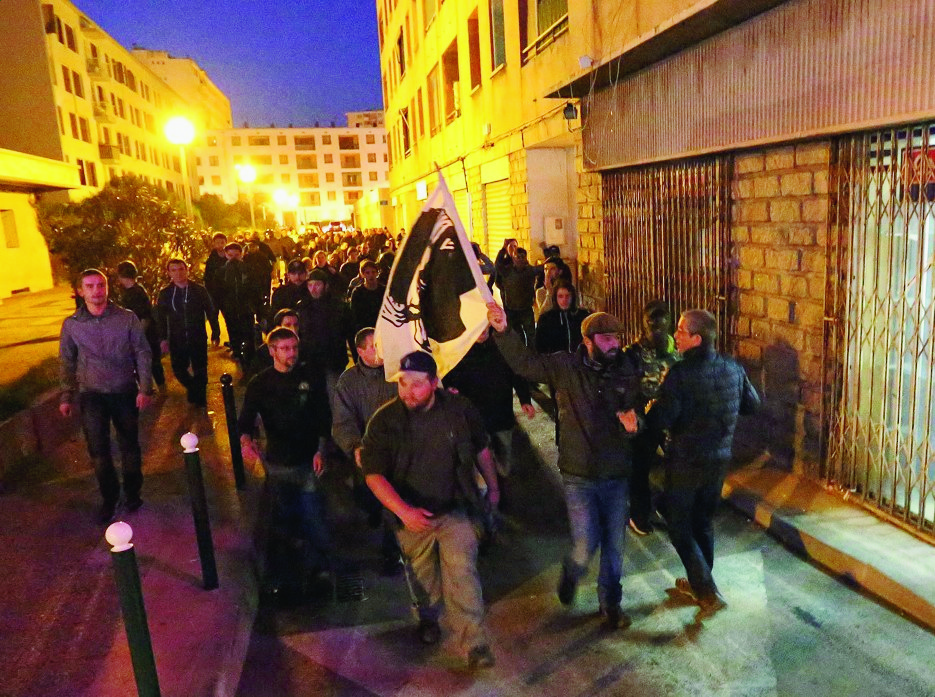 FILE - This Saturday, Dec. 26, 2015 file photo shows demonstrators, most of them angry against Muslim residents, marching behind the Corsican flag in Ajaccio, on the French Mediterranean island of Corsica. Frances interior minister is seeking to halt violence in Corsica after protesters vandalized a Muslim prayer room in anger over an ambush of firefighters. Bernard Cazeneuve, visiting the Corsican city of Ajaccio on Wednesday, told reporters there is no place in Corsica for violence or racism. (AP Photo/Jean-Pierre Belzit, File) France Corsica