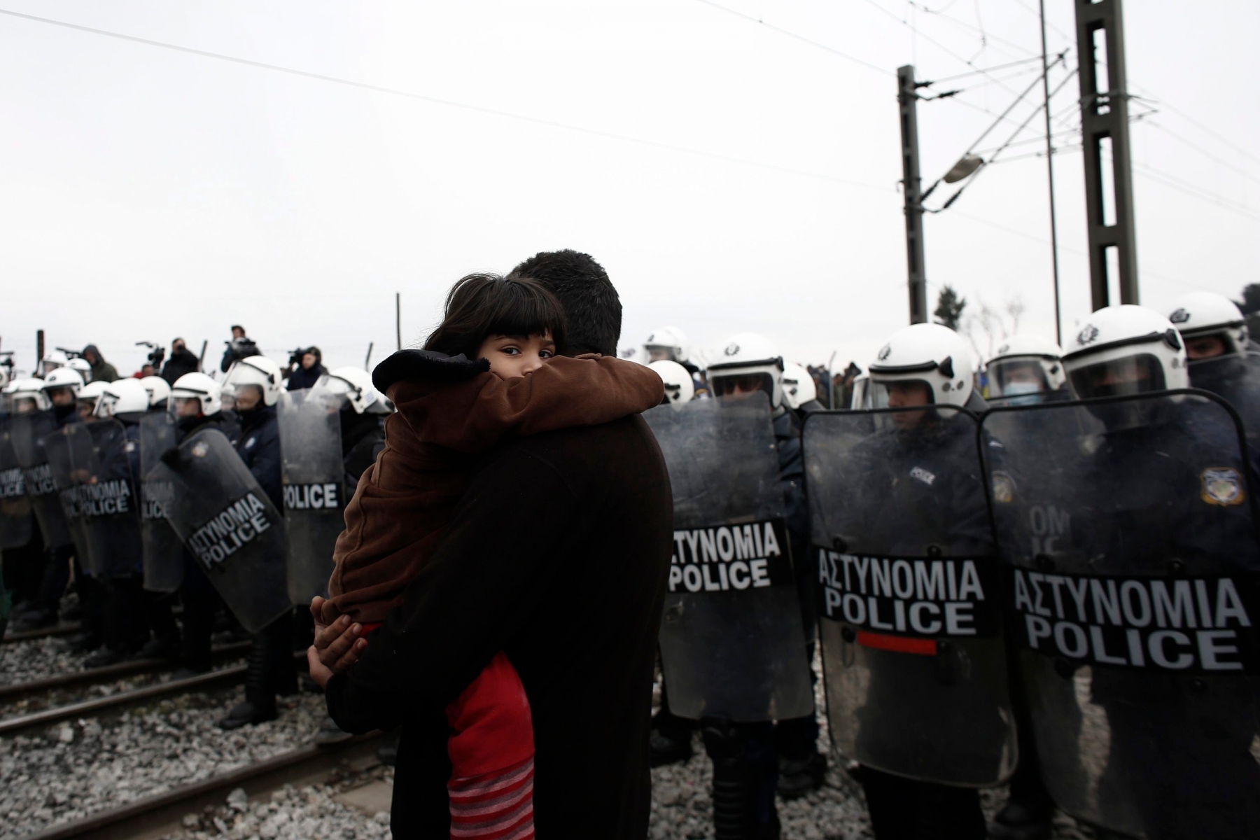 epa05232701 A Syrian refugee child looks as her father carry her in front of riot police during a protest organised by refugees and migrants demanding the opening of the borders at the refugee camp of Idomeni near the Greek-Former Yugoslav Republic of Macedonia (FYROM) borders in northern Greece, 27 March 2016. Migration restrictions along the so-called Balkan route, the main path for migrants and refugees from the Middle East into the European Union, has left thousands of migrants trapped in Greece.  EPA/KOSTAS TSIRONIS GREECE REFUGEES MIGRATION CRISIS
