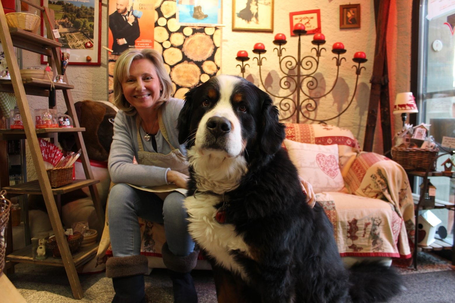 8 mars 2016. Saint-Prex. Dany-Chantal Monnier cherche un repreneur pour son commerce La Belle Suisse situé dans l'ancienne forge, à côté de l'horloge. Elle officie aussi comme office du tourisme. Son chien Jazz  est souvent pris en photo par les touristes. Il fait partie intégrante de cette boutique qui vend du fromage et des produits du terroir. Photo: Fabienne Morand