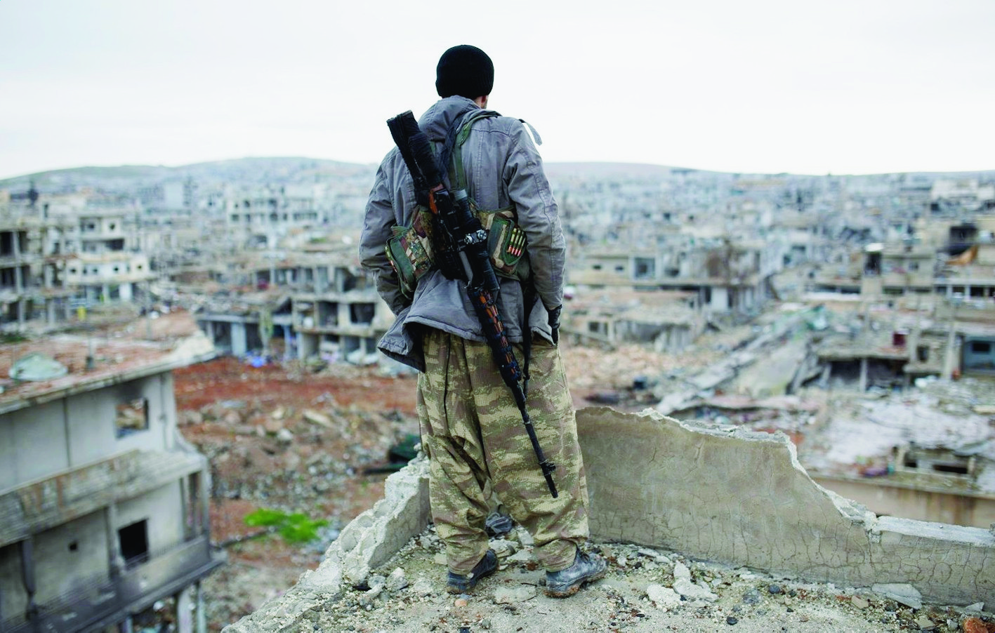 FILE - In this Jan. 30, 2015 file photo, a Syrian Kurdish sniper looks at the rubble in the Syrian city of Ain al-Arab, also known as Kobani. Foreign fighters are streaming in unprecedented numbers to Syria and Iraq to battle for the Islamic State or other U.S. foes, including at least 3,400 from Western nations and 150 Americans, U.S. intelligence officials conclude. In all, more than 20,000 fighters have traveled to Syria from more than 90 countries, top intelligence officials will tell Congress this week.  (AP Photo, File) Islamic State Foreign Fighters