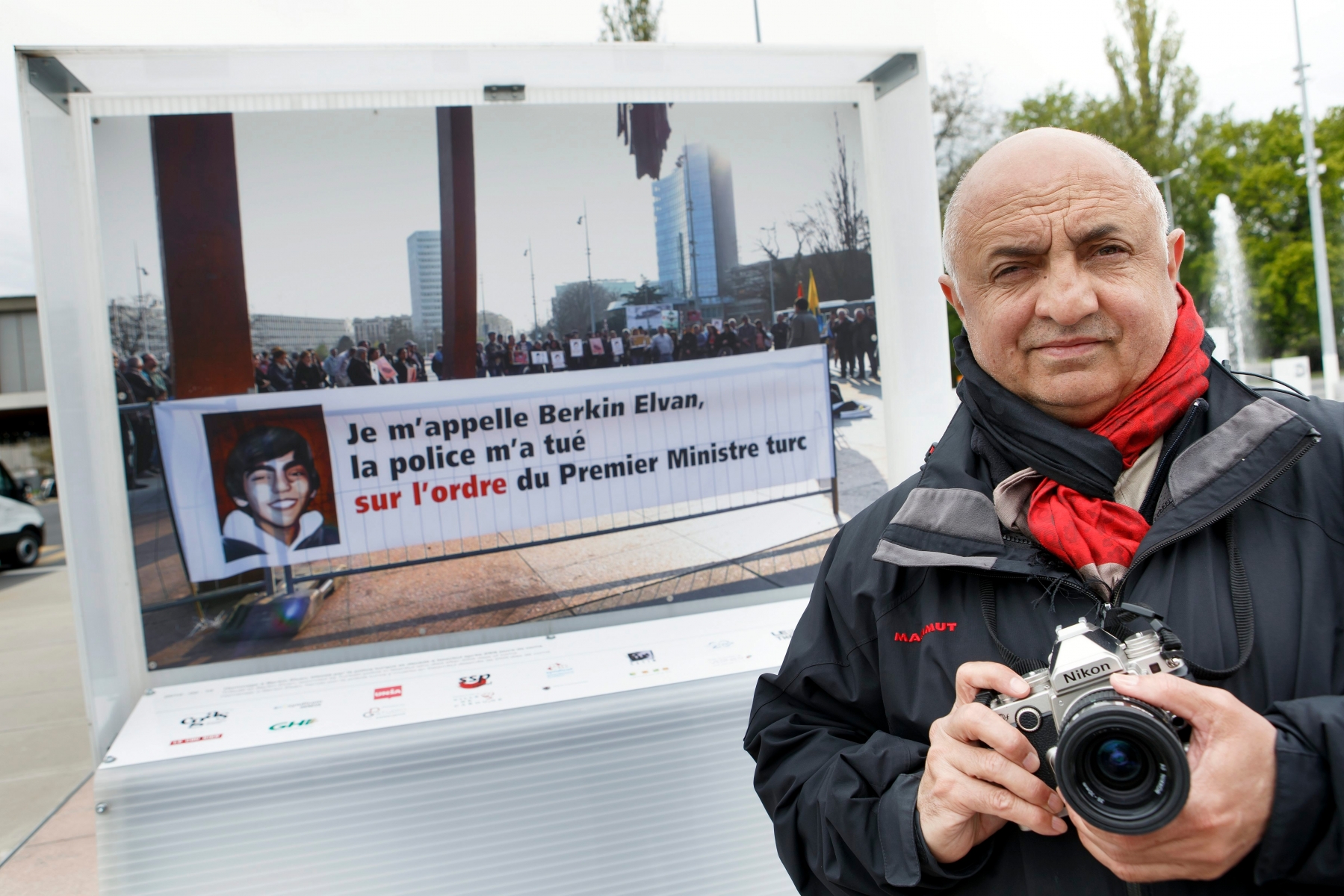 Geneva's Kurdish and Armenian photographer Demir Soenmez poses for the media next to his picture with caption "Tribute to Berkin Elvan, wounded by Turkish police in Istanbul who died after 269 days of coma" displayed on the Place des Nations in front of the European headquarters of the United Nations in Geneva, Switzerland, Monday, April 25, 2016. A photo displayed on the Place des Nations, which calls into question the current Turkish President Recep Tayyip Erdogan angered Turkey. Its consulate requested the withdrawal of the picture. The city of Geneva will focus Tuesday on the request. The Geneva's Kurdish and Armenian photographer Demir Soenmez exposes until Sunday 58 photos of events on the Place des Nations. Among them was a banner in March 2014 which made responsible Erdogan, Prime Minister, of the death of a teenager during a protest in Istanbul. (KEYSTONE/Salvatore Di Nolfi) SWITZERLAND PICTURE EXHIBITION