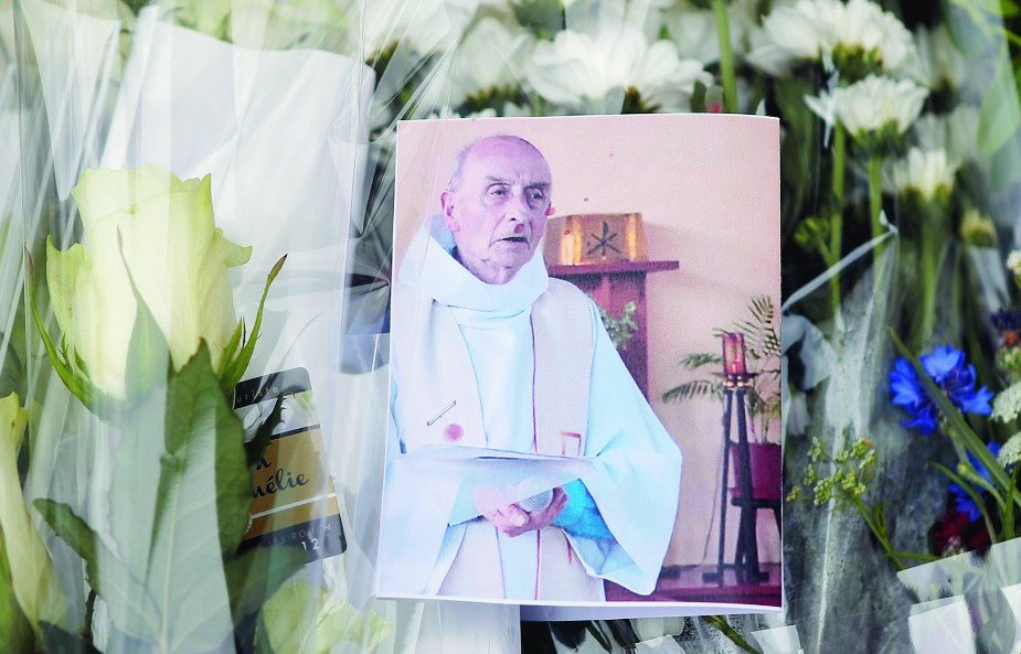 A picture of late Father Jacques Hamel is placed on flowers at the makeshift memorial in front of the city hall closed to the church where an hostage taking left a priest dead the day before in Saint-Etienne-du-Rouvray, Normandy, France, Wednesday, July 27, 2016. The Islamic State group crossed a new threshold Tuesday in its war against the West, as two of its followers targeted a church in Normandy, slitting the throat of an elderly priest celebrating Mass and using hostages as human shields before being shot by police. (AP Photo/Francois Mori) France Hostage Taking