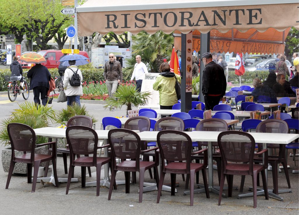 Gaeste sitzen in einem Lokal auf der Piazza Grande in Locarno, am Ostersamstag, 7. April 2012. Obwohl die Temperaturen genug hoch sind um draussen zu sitzen, macht das regnerische Wetter den Besuchern und Restaurantbesitzern einen Strich durch die Rechnung. (KEYSTONE/Karl Mathis)