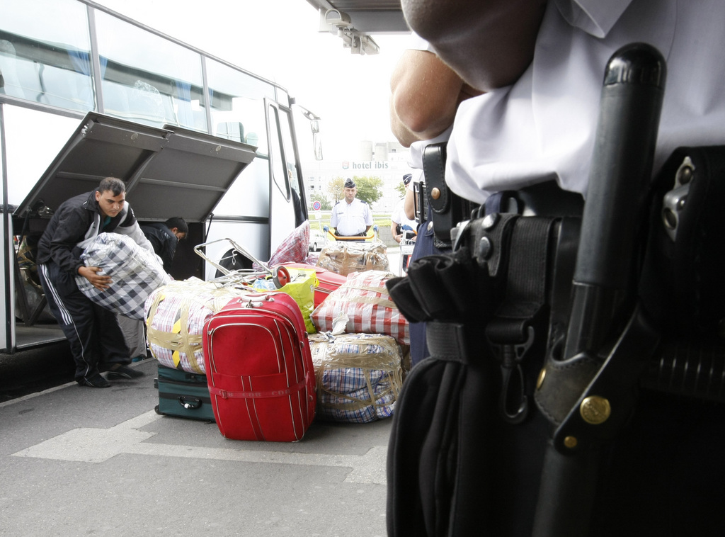 A police officer watches as Roma unload their luggage from a bus, before being expelled from France at Roissy airport, north of Paris, Thursday  Aug. 26 2010. The Archbishop of Paris, Andre Vingt-Trois has added to mounting criticism of the French government's crackdown on Gypsies, or Roma, calling it a "circus." A poll says the French are split on the issue, and meanwhile the government puts more Roma on planes home to Eastern Europe. Citizens of Romania and Bulgaria, both EU member states, benefit from free circulation within the bloc, but the French labour market is not fully open to them and if they do not have a job and lodging after three months they are required to leave the country(AP Photo/Jacques Brinon)